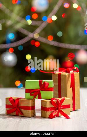 Gift boxes with red bows. Christmas tree with blurred twinkling party lights and toy balls on the background. Christmastime celebration. Stock Photo