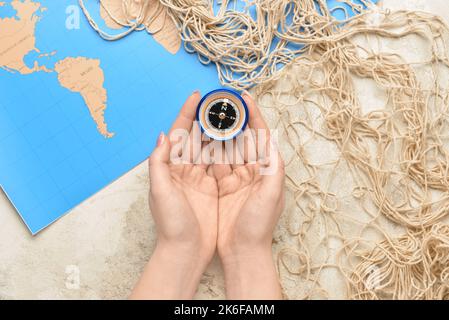 Female hands with compass, fishnet and world map on light background Stock Photo