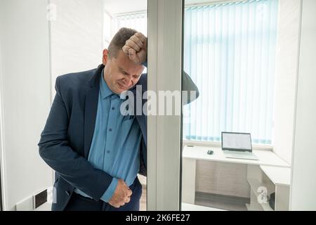 A businessman is suffering from pain in the office. Excruciating abdominal pain. The employee is overworked. The concept of overwork at work and fatig Stock Photo