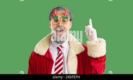 Happy bearded man in funny Christmas glasses and Santa coat has good idea and points finger up Stock Photo