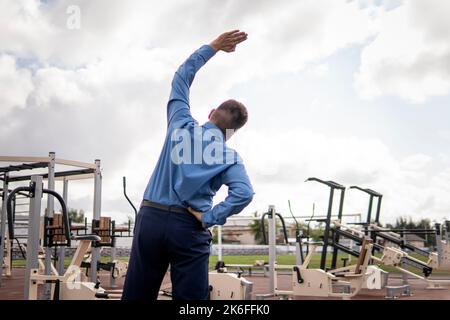 Businessman doing exercises in the gym. a man in a business suit does exercises at the stadium. Stock Photo