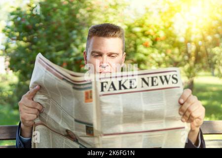 Close-up Of An Man Reading Fake News On Newspaper sitting on a bench in the park Stock Photo