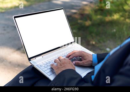 Young hipster student using laptop on grass in park at sunset. Blank white screen copy space. View over the shoulder. male programmer works against th Stock Photo