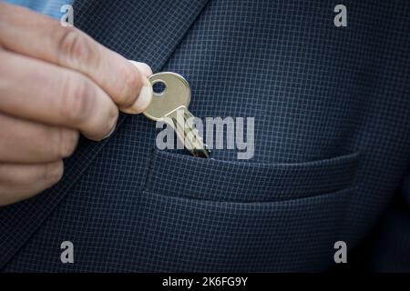 a businessman puts a small key to a safe deposit box or a bank in his jacket pocket the concept of saving money. The real estate agent takes out the k Stock Photo