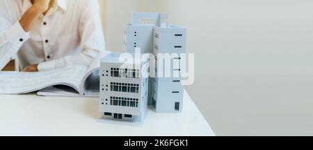 panoramic wide banner with copy space. building model on workplace desk with architect or construction worker working with blueprint on desk in office Stock Photo