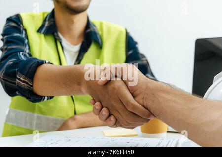 group of architect, engineer construction worker team hands shaking after plan project contract with blueprint and document on desk in office at const Stock Photo