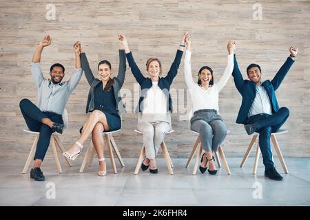 We win together, we lose together. Full length shot of a diverse group of businesspeople sitting together and holding hands while raising them. Stock Photo