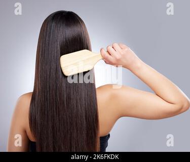 Regular hair brushing will make it sleek, shiny and manageable. Rearview shot of a young woman combing her hair against a grey background. Stock Photo