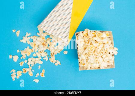 Snack concept, Sweet popcorn in paper cup and spill out from paper cup on light blue background. Stock Photo