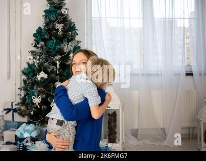 mom and little son 4-6 years old on the background of Christmas tree, gently hug each other. cozy family new year holidays at home. Magical Christmas Stock Photo