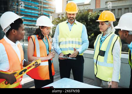 Ive got the clients plans right here. a diverse group of contractors standing outside together and having a discussion over building plans. Stock Photo