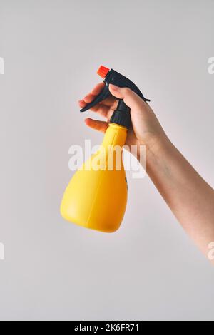 A young woman holds a spray bottle in her hand. Yellow spray bottle on white background  Stock Photo
