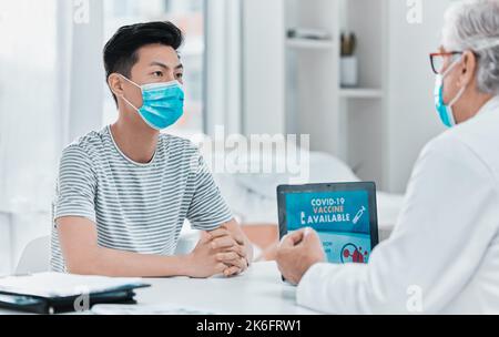 We offer Covid vaccines here. a young man wearing a face mask and sitting with his doctor during his consultation in the clinic. Stock Photo