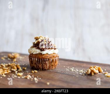 Tasty chocolate muffin with creme mascarpone and chocolate on top, covered with nuts. Placed on wooden desk. Sweet fresh and homemade cupcake. Stock Photo