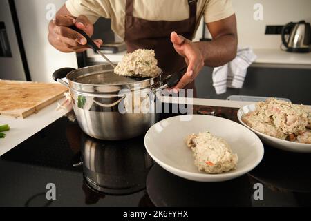Unrecognizable young black man preparing boiled chicken mince with vegetables. Stock Photo