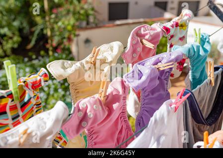 Cloth diapers hanging while drying under the sun on clothesline. Laundry of colorful reusable nappies for babies. Stock Photo