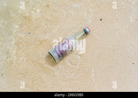 Koh Lipe, Thailand - 13.11.2019: Empty glass from limonade drink is placed on sand beach near sea, at Ko Lipe island, Thailand. Glass garbage pollutio Stock Photo