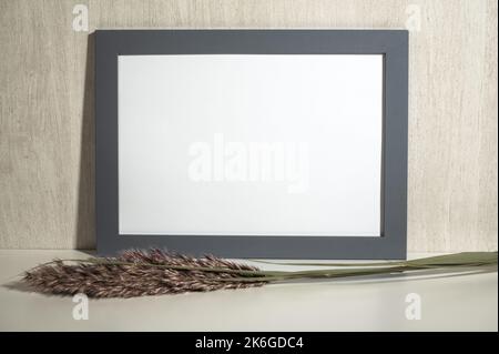 Horizontal grey frame mockup on vintage . Empty grey wooden frame stands on white table with dry grass . Mockup poster frame in home interior. Minimal Stock Photo