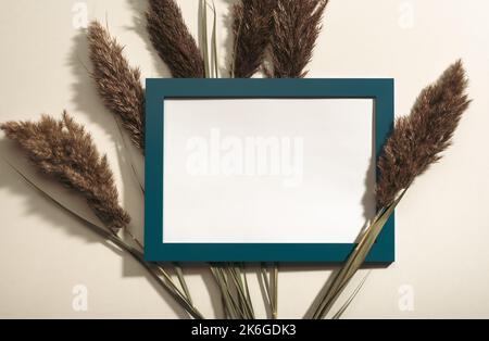 Photo Frame mockup, dried branch grass on beige background. Flat lay, top view, copy space, mockup. Blue Frame with Blank white paper and pampas grass Stock Photo