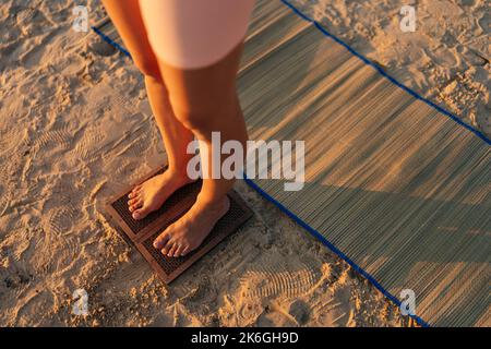 Close-up cropped shot of unrecognizable yogi woman standing barefoot on wooden Sadhu nail board during concentration meditation practice on sandy Stock Photo