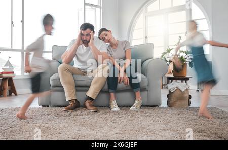 I cant believe you let it go this far. a young couple looking stressed at home while their kids play around them. Stock Photo