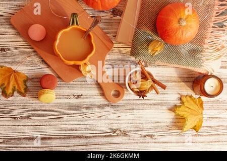 Seasonal pumpkin latte in shape of pumpkin cup among desserts and leaves, Lagom, cozy home. Stock Photo