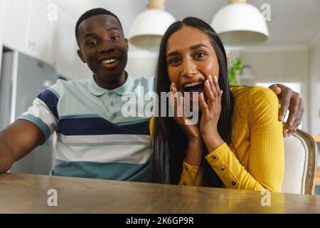 Happy diverse couple making video call smiling and laughing to camera in kitchen Stock Photo