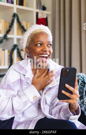 Happy african american woman wearing santa claus hat, using smartphone for video call Stock Photo