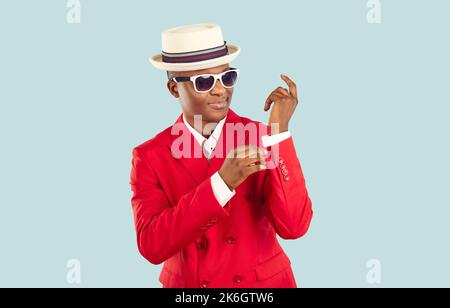 Young trendy African American man in red suit and hat standing in pastel blue studio Stock Photo