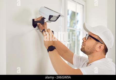 Worker installs security camera with LED light on wall. Stock Photo