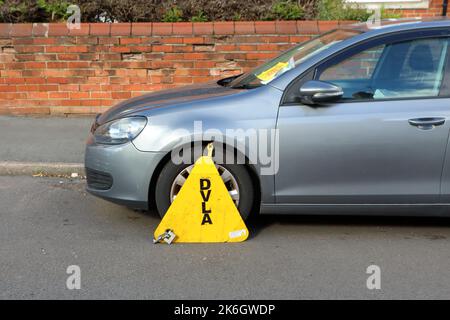 a silver grey car clamped for being untaxed on a side street Stock Photo