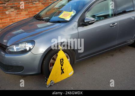 a silver grey car clamped for being untaxed on a side street Stock Photo