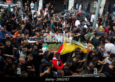 Jenin, Palestine. 14th Oct, 2022. (EDITORS NOTE: Image depicts death)Mourners and gunmen carry the body of 18-year-old Palestinian gunman Matin Dabbaya, who was killed during clashes with the Israeli army in the Jenin refugee camp near the city of Jenin in the occupied West Bank. The Israeli army stormed the Jenin refugee camp to arrest a wanted man. The Palestinian Ministry of Health said that a Palestinian was killed and 14 others, including a doctor, were wounded during this military operation. Credit: SOPA Images Limited/Alamy Live News Stock Photo