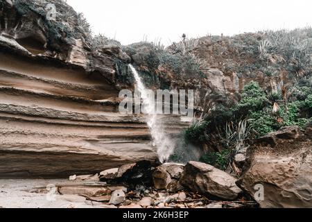 small waterfall with little water pushed by the force of the wind coming down from the large rocks with curious shapes on the stones and rocks among Stock Photo