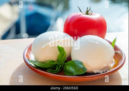 White soft italian mozzarella bufala cheese in balls with red tomato and basil served outdoor Stock Photo