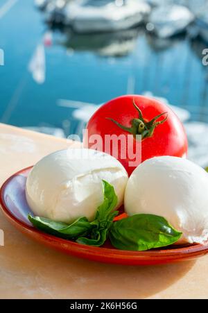 White soft italian mozzarella bufala cheese in balls with red tomato and basil served outdoor Stock Photo