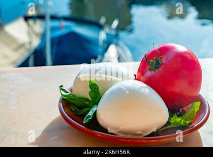 White soft italian mozzarella bufala cheese in balls with red tomato and basil served outdoor Stock Photo