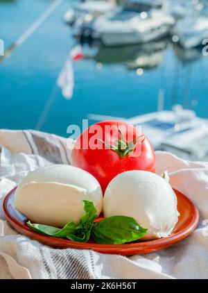 White soft italian mozzarella bufala cheese in balls with red tomato and basil served outdoor Stock Photo