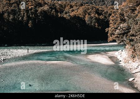 young caucasian man on the shore of a stony calm shallow river with transparent waters in a very bright environment among the vegetation and trees of Stock Photo