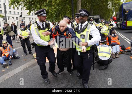 Police officers detain a Just Stop Oil protester outside New Scotland Yard in London. Picture date: Friday October 14, 2022. Stock Photo