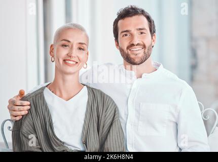 Portrait of happy young caucasian couple posing together seated on a chair in their home. Man sitting with his arm around his wife. Happy and healthy Stock Photo