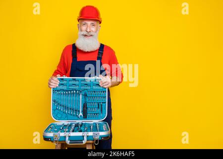 Photo of happy smiling age man wear overall uniform red hard hat holding toolkit empty space isolated yellow color background Stock Photo