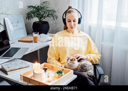 Relaxed young woman with cat sitting near table with burning candles and aroma sticks at home and do meditation and relaxation Stock Photo