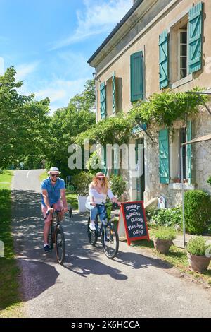 Couple riding bikes on the banks of the Canal du Midi in front of the lock keeper’s house converted into a restaurant and bed and breakfast called “La Stock Photo