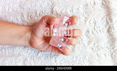 Girl with halloween themed nails on fluffy white blanket holding rose quartz. Aesthetic Isolated on white surface. Nails with ghosts and eyes Stock Photo