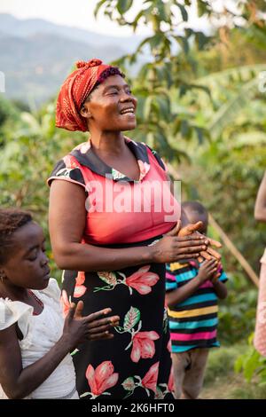 A happy African woman sings with her family outside her home in Uganda's Rwenzori Mountains, Kasese District, East Africa. Stock Photo