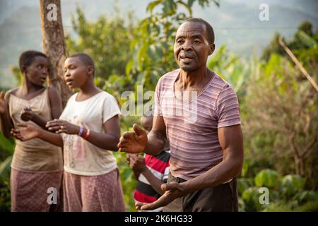 A happy African man sings with his family outside her home in Uganda's Rwenzori Mountains, Kasese District, East Africa. Stock Photo