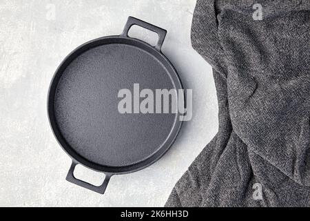 Black cast iron empty frying pan and gray kitchen towel on a gray concrete background Stock Photo