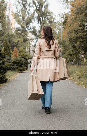 back view of woman in trench coat walking on street of european city ...