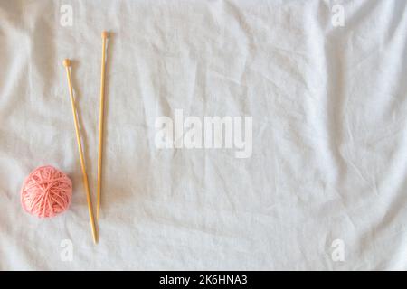 Pink thread ball with wooden bamboo knitting needles on white linen fabric background. Top view, copy space. Hobby, relaxation, mental health Stock Photo